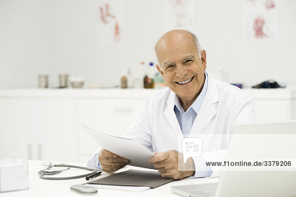 Arzt am Schreibtisch lächelnd vor der Kamera  Porträt