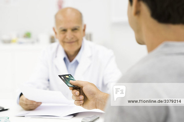 Patient übergibt Kreditkarte an Arzt