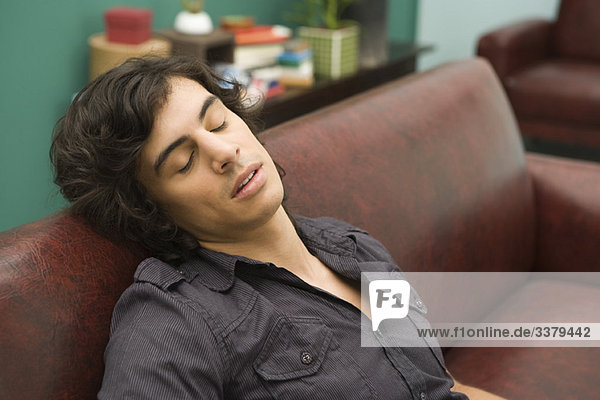 Young man dozing off to sleep on sofa