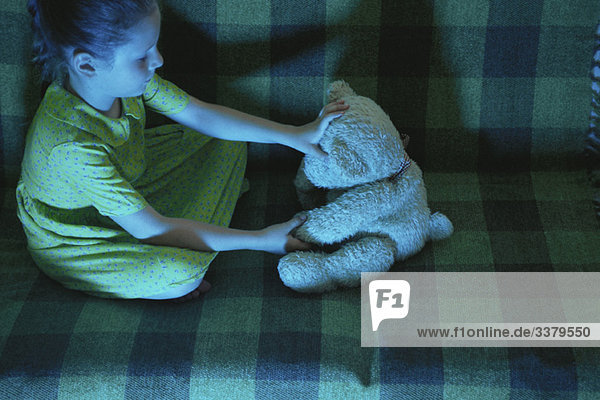 Kleines Mädchen sitzt auf dem Sofa mit Teddybär
