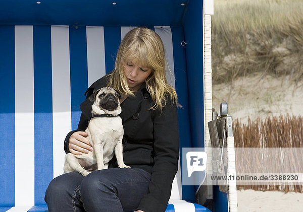 Pug puppy sitting on lap of teenage girl in beach chair  Sylt  Schleswig-Holstein  Germany