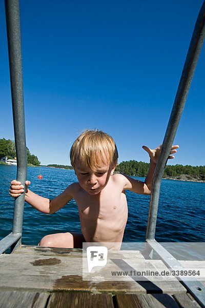 Junge auf einer schwimmen Leiter unter einem klaren  blauen Himmel  Schweden.
