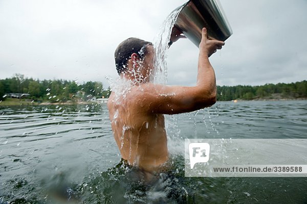 Man standing in the water pouring water over himself from a bucket  Sweden.