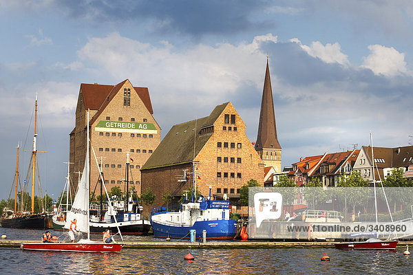 View of warehouses and St. Peter's Church  boats on a river in the foreground  Rostock  Germany