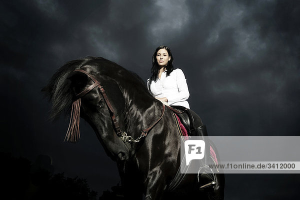 Junge Frau reitet auf einem schwarzen Pferd