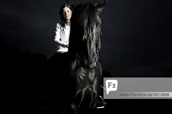 Junge Frau reitet auf einem schwarzen Pferd