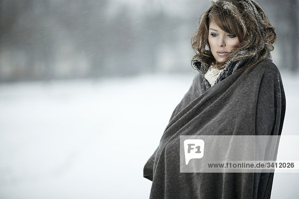 Junge Frau steht mit Poncho im Schnee