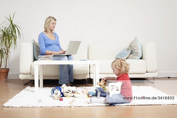 Frau auf einem Laptop zu Hause mit Kleinkind