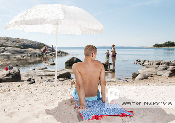 Mann am Strand unter einem Sonnenschirm sitzend