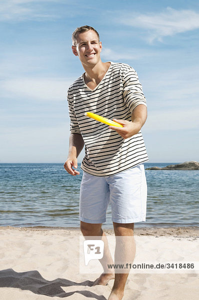 Ein Mann am Strand hält ein Frisbee.