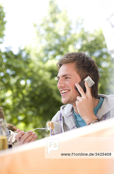Junger Mann telefoniert mit einem Handy beim Essen  Flachwinkelansicht