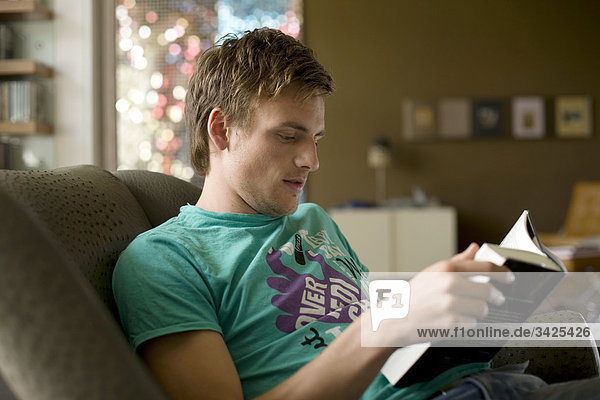 Junger Mann sitzt auf einer Couch und liest ein Buch