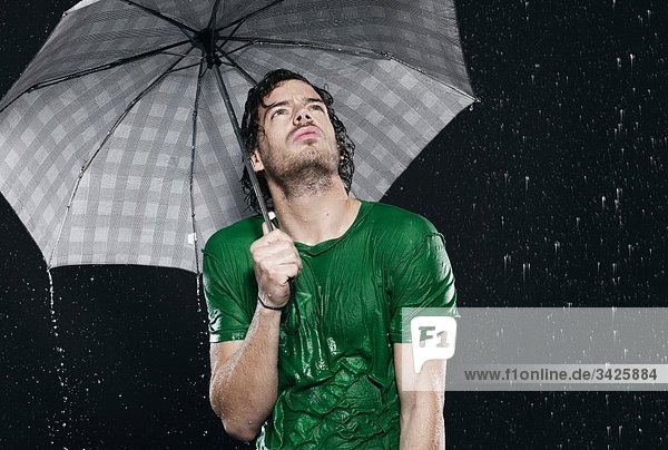 Mann steht im Regen  hält Regenschirm.