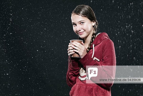 Girl standing in rain  holding disposable cup.