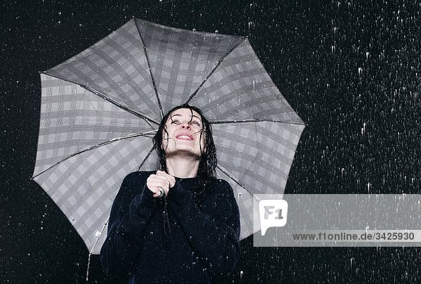 Frau steht im Regen  hält Regenschirm.