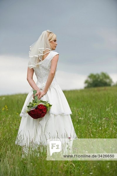 Die Braut hält einen Blumenstrauß hinter ihrem Rücken und schaut weg.