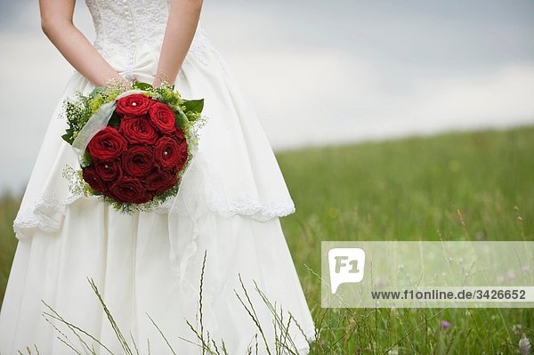 Braut auf der Wiese stehend mit Blumenstrauß  Mittelteil  Nahaufnahme