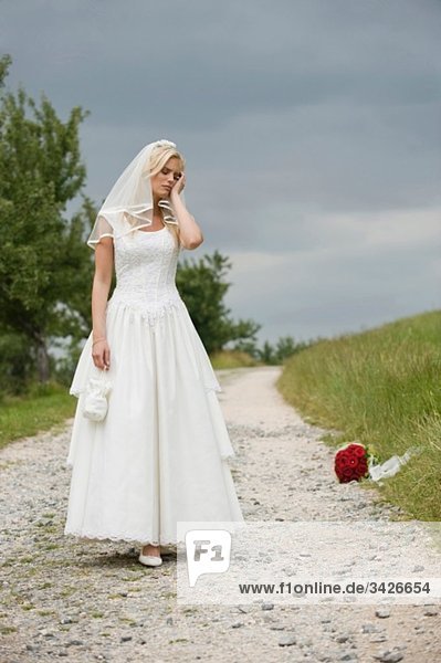 Die Braut steht auf einem Feldweg.