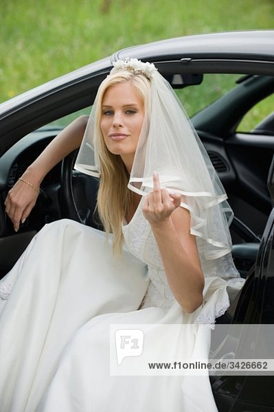 Die Braut sitzt in einem Auto und zeigt ihren Finger.