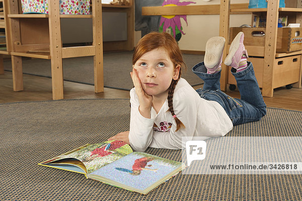Germany  Girl (6-7) in nursery lying on carpet reading a book