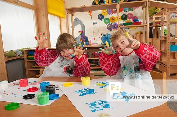 Germany  Two boys (3-4)  (6-7) fingerpainting in nursery  showing hands  smiling  portrait