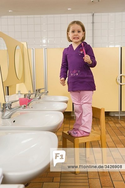 Deutschland  Mädchen (3-4) stehend auf Stuhl in der Toilette mit Zahnbürste  Seitenansicht  Porträt