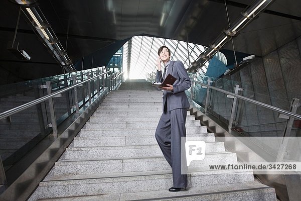 Geschäftsfrau mit Handy an der U-Bahn-Station  auf der Treppe stehend
