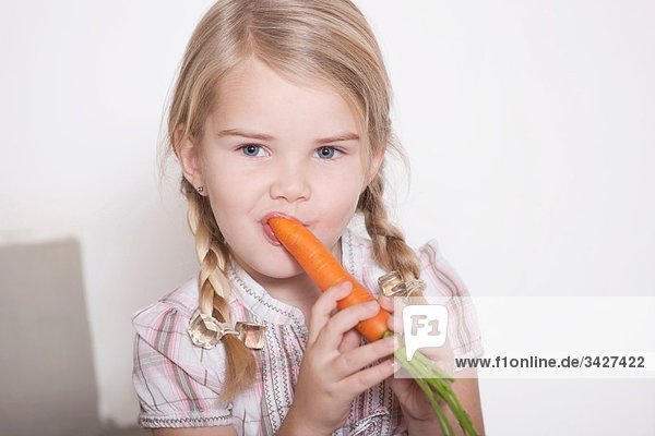 Girl (4-5) with braids eating a carrot portrait close-up
