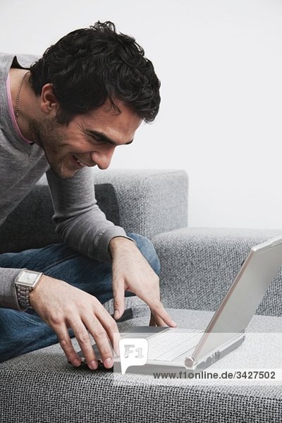 Man sitting on sofa using laptop  smiling