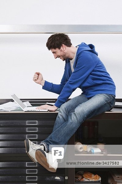 Man sitting on desk using laptop  gesturing