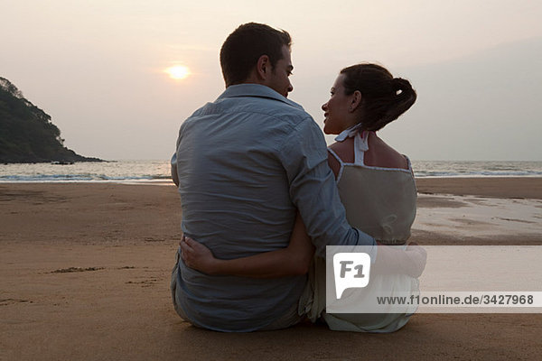 Paar sitzt am Strand bei Sonnenuntergang