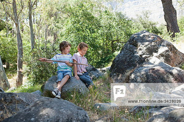 Boys sitting on rocks with stick