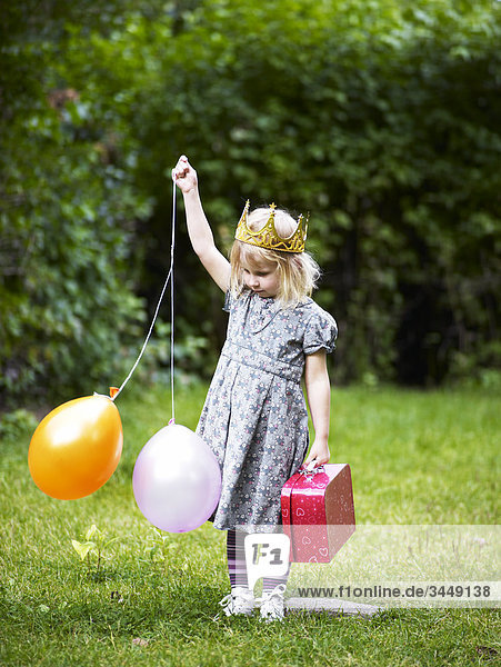 Scandinavia  Sweden  Stockholm  Girl wearing crown standing in park holding balloons and bag