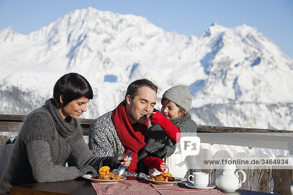 Paar und Tochter beim Essen auf dem Balkon im Skigebiet