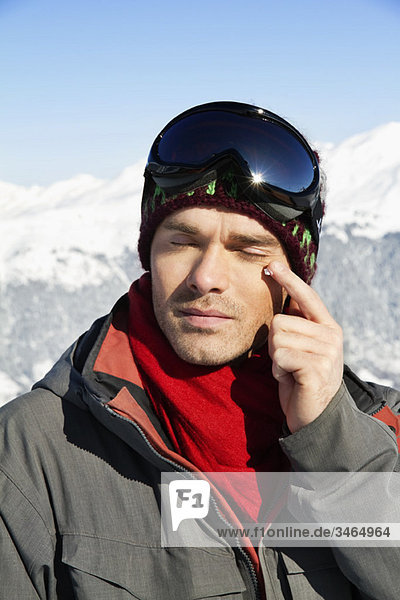 Young man in ski wear applying moisturizer on his face