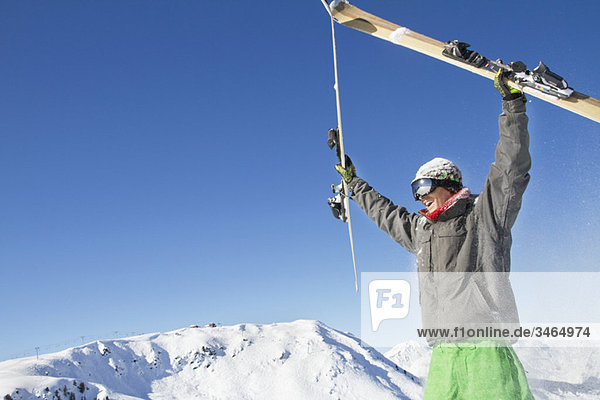 Junger Mann hält seine Skier über den Kopf.