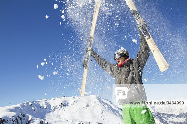 Junger Mann hält seine Skier über den Kopf.