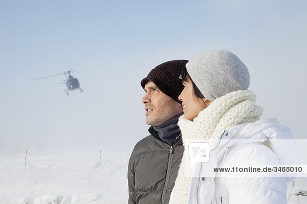 Young couple in winter clothes,  helicopter in background