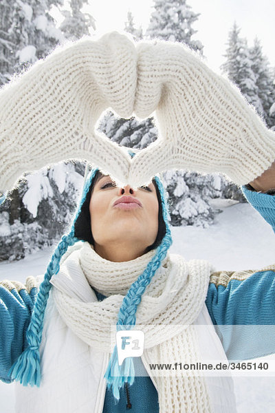 Young woman in winter clothes making heart shape with hands