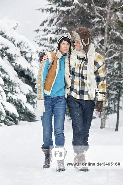 Junges Paar umarmend  im Schnee spazieren gehend