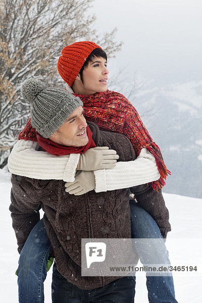 Young man giving his girlfriend piggyback in snow