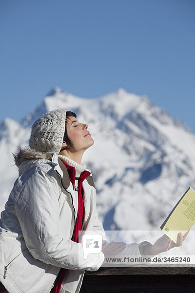 Young woman with book  enjoying winter sun  mountains in background