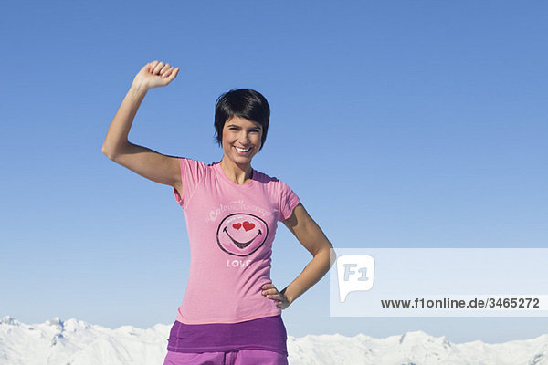 Young woman with arm raised  smiling at camera  mountains in background