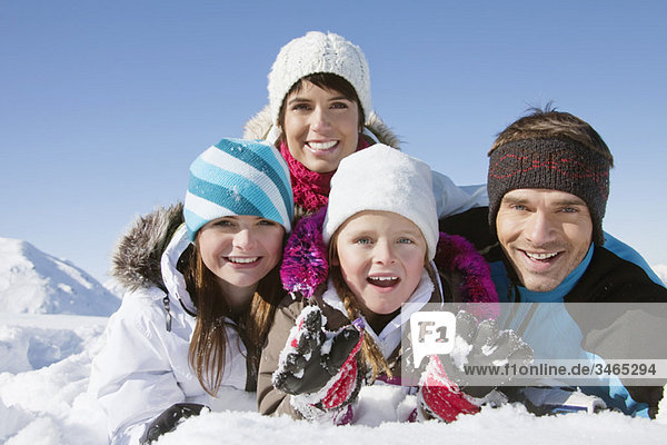 Parents and children lying in snow  smiling at camera