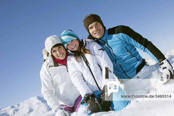Couple and daughter sitting in snow  smiling at camera