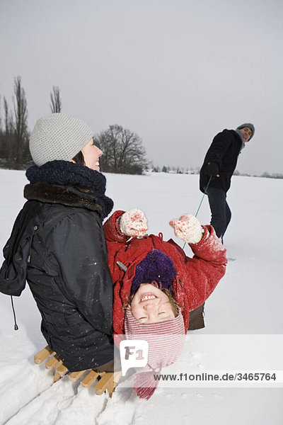 A man pulling a sled with his wife and daughter on it
