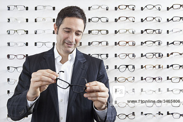 Ein reifer Mann der eine Brille in einem Brillengeschäft auswählt.