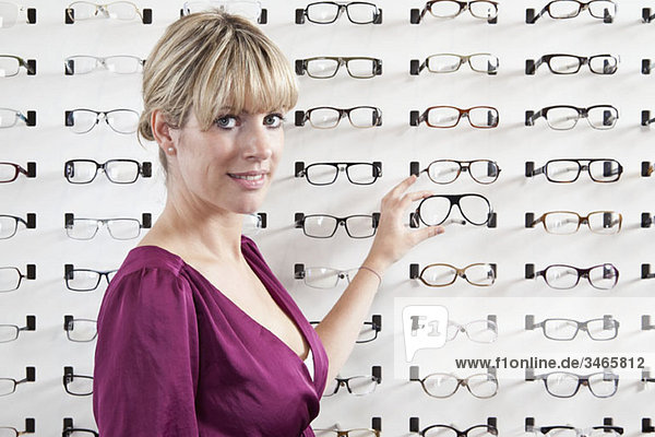 Eine mittlere erwachsene Frau  die eine Brille in einem Brillengeschäft auswählt.
