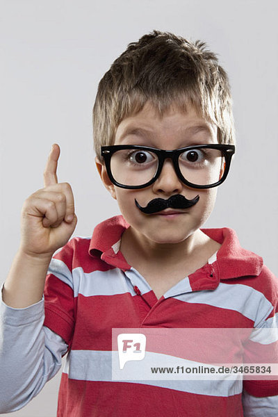 Ein junger verspielter Junge mit einer falschen Brille und einem falschen Schnurrbart.