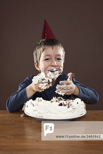 Ein Junge mit einem Partyhut  der Kuchen mit den Händen isst  Studioaufnahme